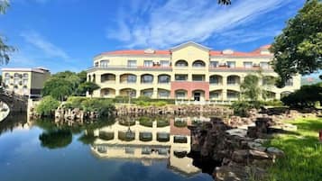 A multi-story hotel with a reflection in the water, a stone bridge, and a red roof.