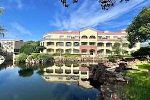 A multi-story hotel with a reflection in the water, a stone bridge, and a red roof.