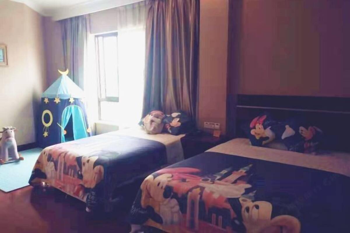 Een hotelkamer met twee bedden, een raam met gordijnen, een klein speeltentje en een nachtkastje met Mickey Mouse beeldjes.