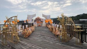 Een houten terras met een decoratieve boog, versierd met bloemen en oranje ballonnen, dat uitkomt bij een mooi uitkijkpunt.