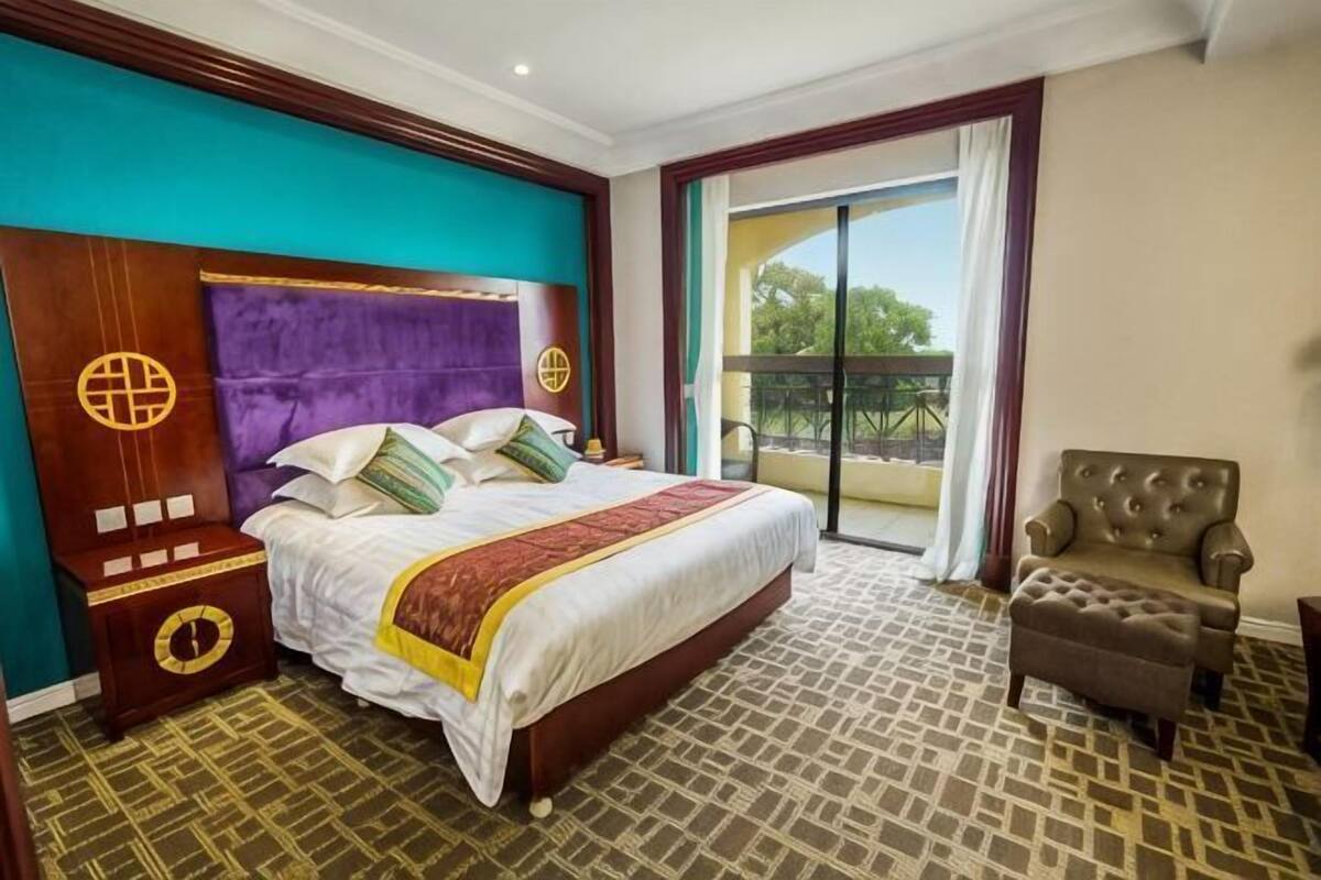 Een hotelkamer met een groot bed, een nachtkastje, een stoel, een balkon met uitzicht en een vloer met een patroon.
