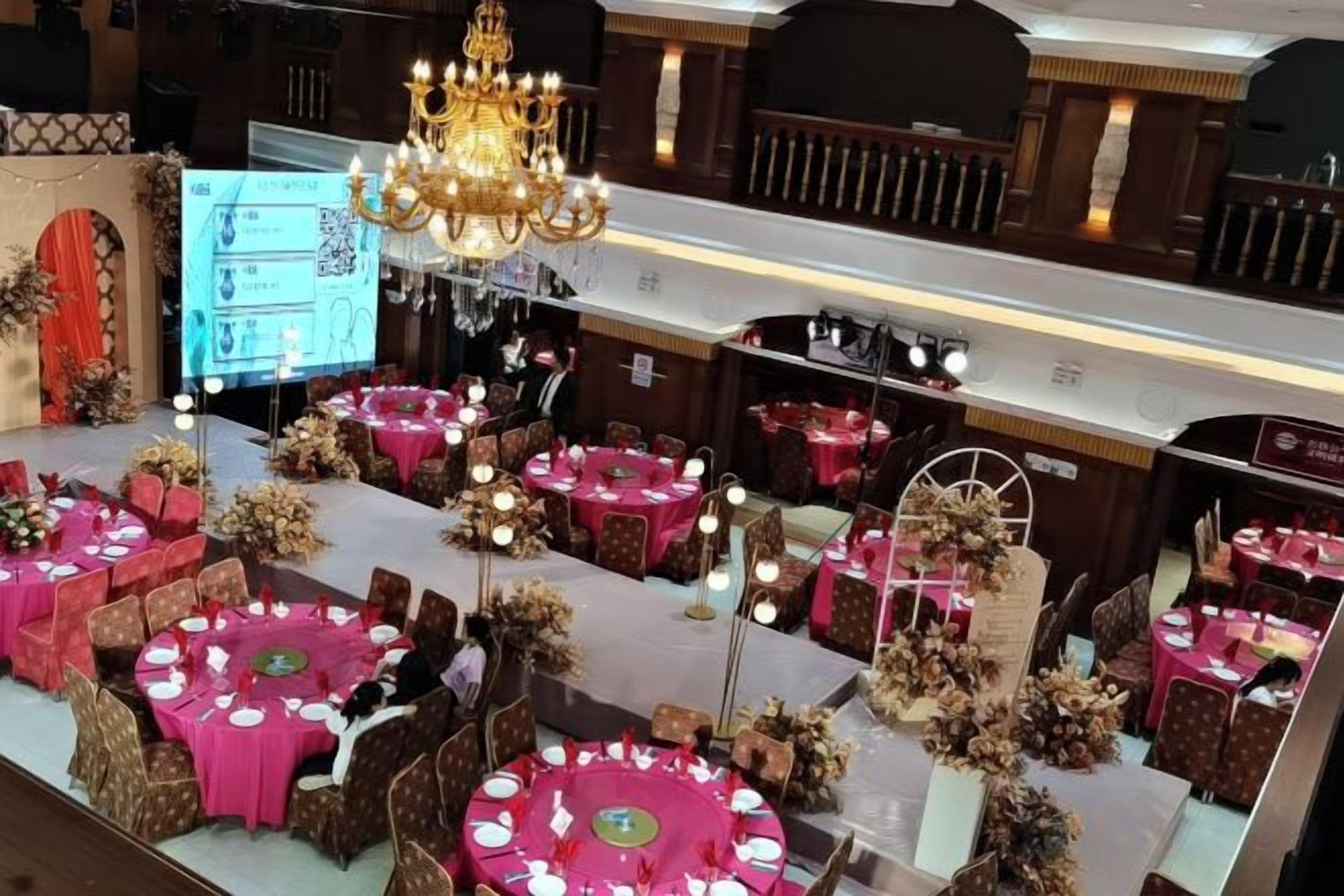 A banquet hall with round tables, chandeliers, and floral centerpieces.