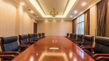 A conference room with a long table and multiple chairs, a chandelier, and large windows with curtains.