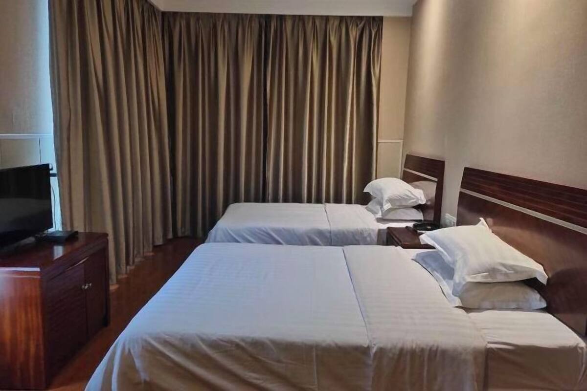 Een hotelkamer met twee bedden, een televisie op een houten kast en een groot raam met gordijnen.