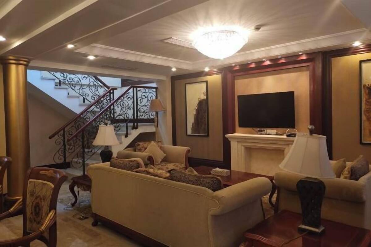Een woonkamer met een bank, fauteuils, een televisie en een open haard.