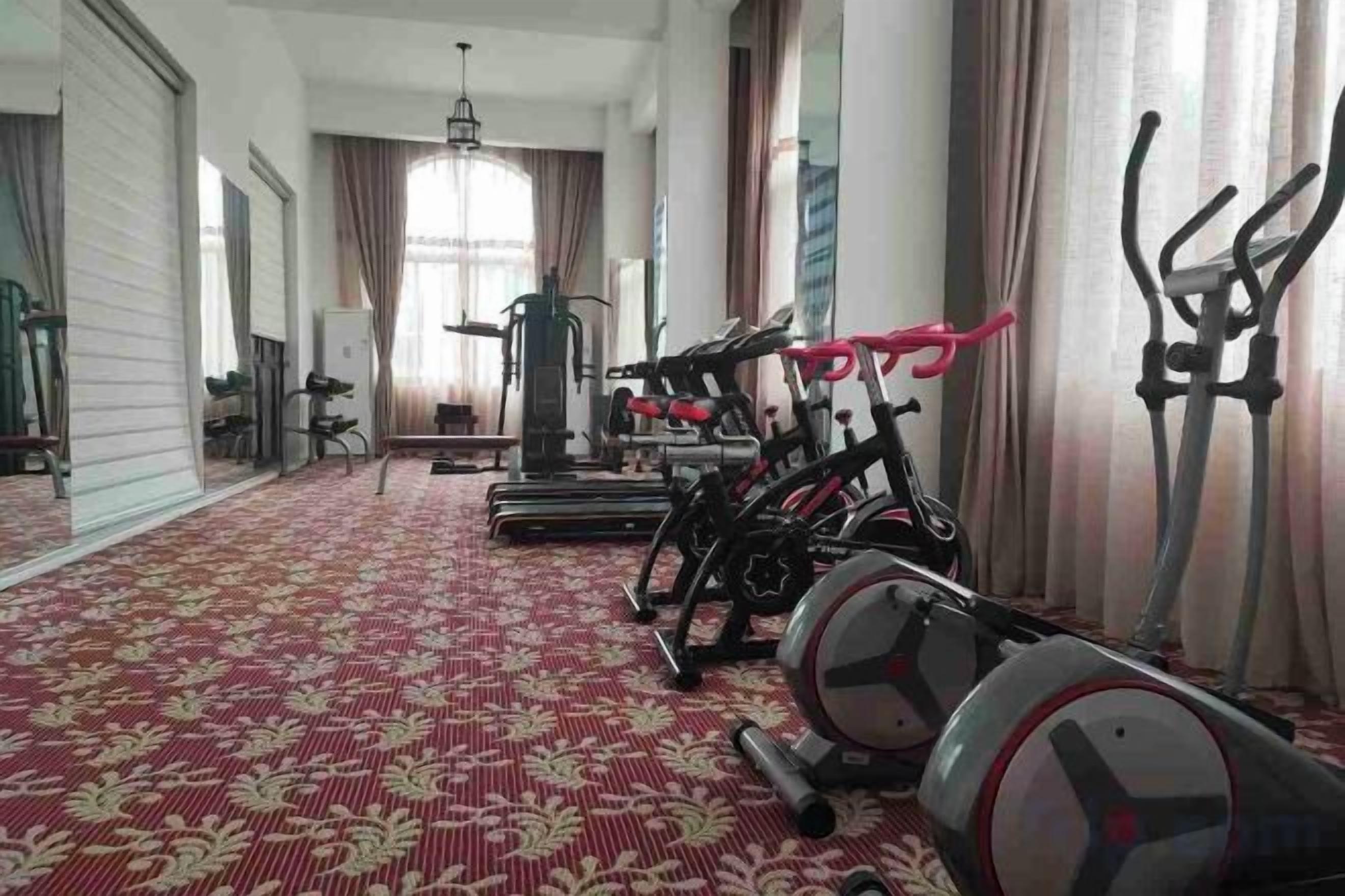 A gym with exercise equipment, a patterned carpet, and large windows with curtains.
