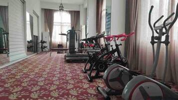 A gym with exercise equipment, a patterned carpet, and large windows with curtains.