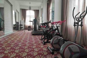 Une salle de sport équipée de matériel d’exercice, dot ée d’un tapis à motifs et de grandes fenêtres avec des rideaux.