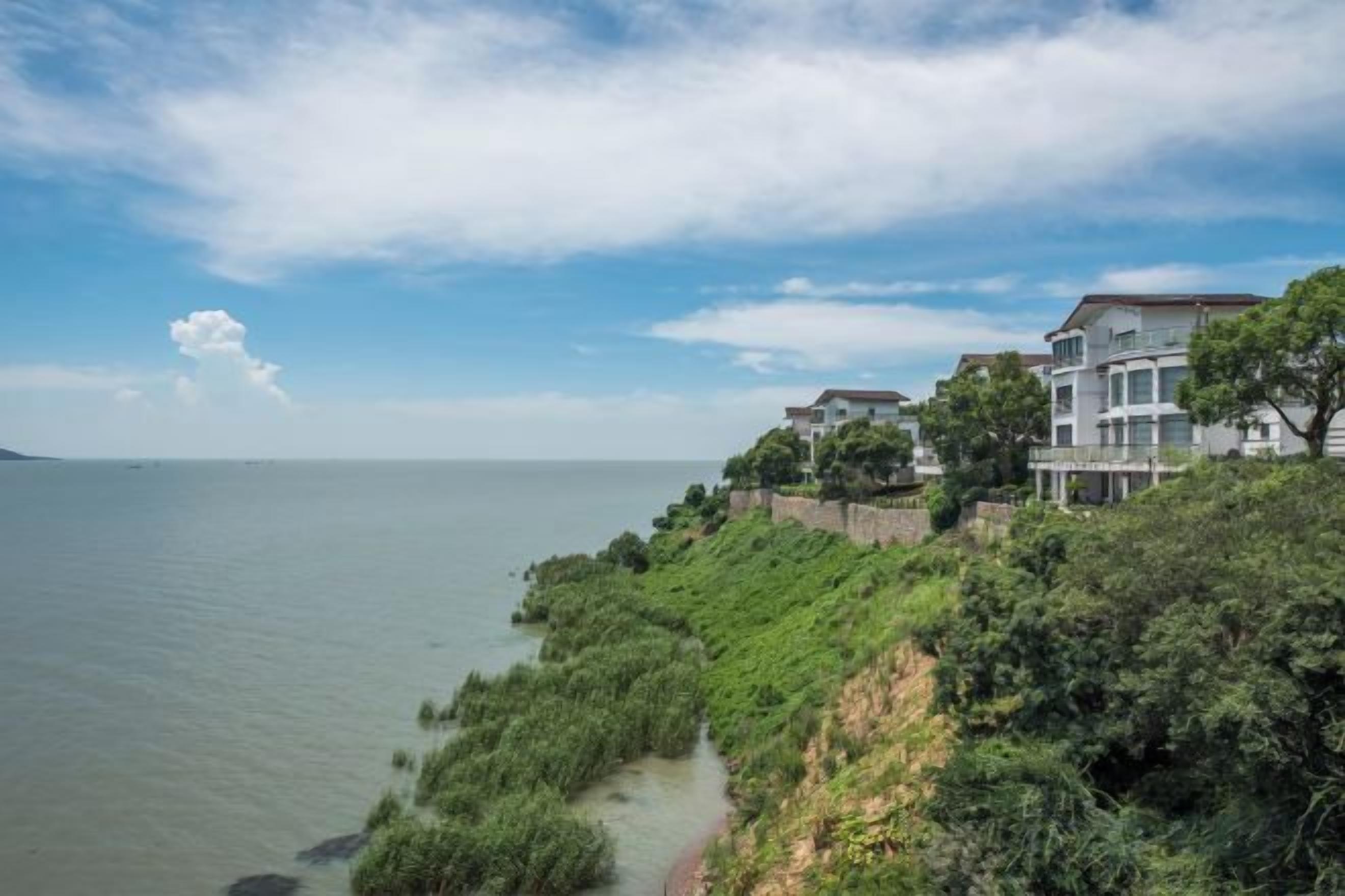 A coastal property with a pathway leading to a building with multiple levels, overlooking a body of water.