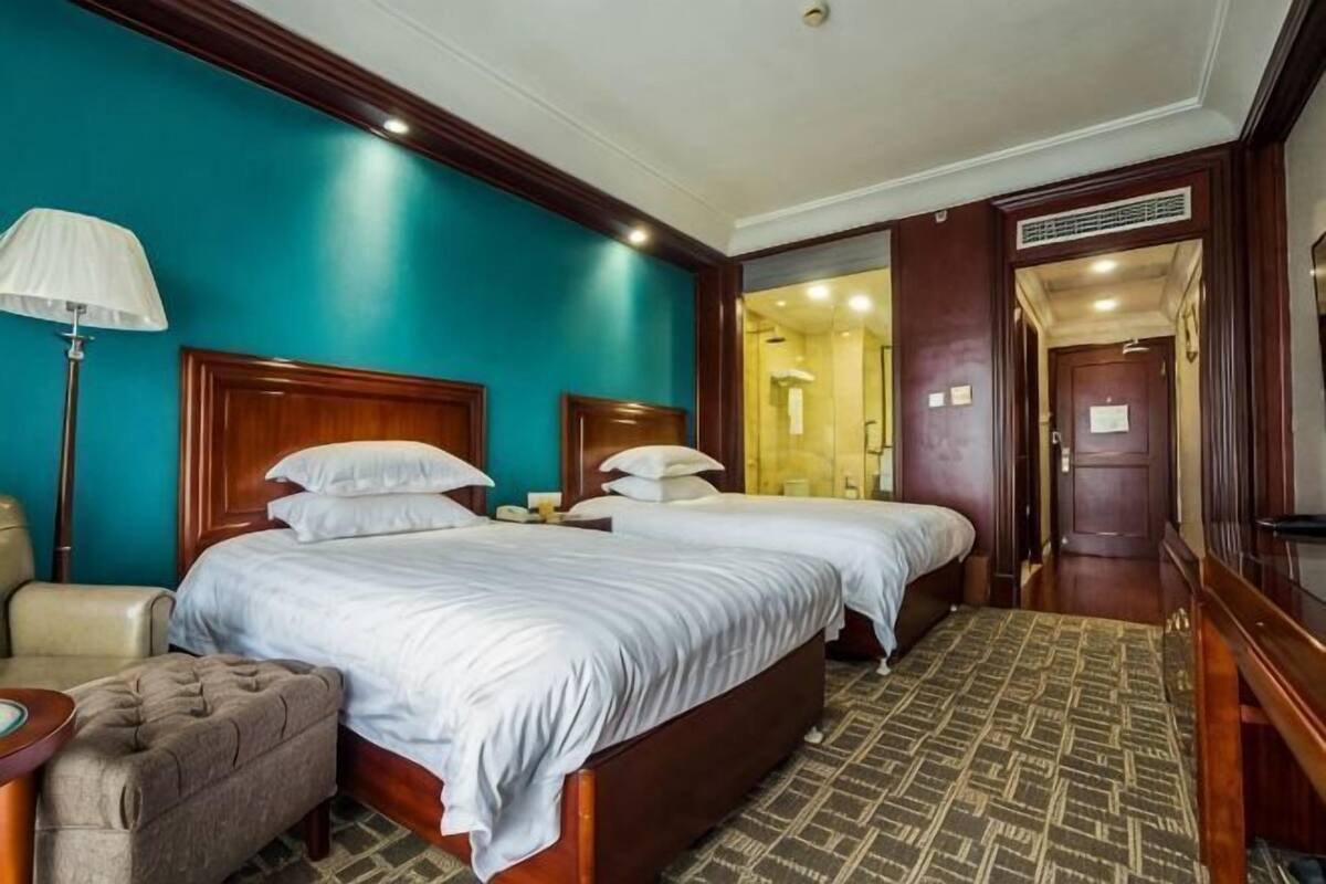 Een hotelkamer met twee bedden, een bureau, een stoel en een badkamer die door een open deur zichtbaar is.
