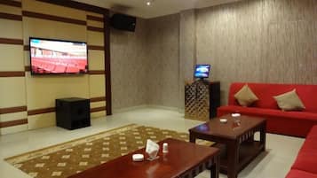 A living room with a flat-screen TV, a red sofa, a wooden coffee table, and a patterned rug.