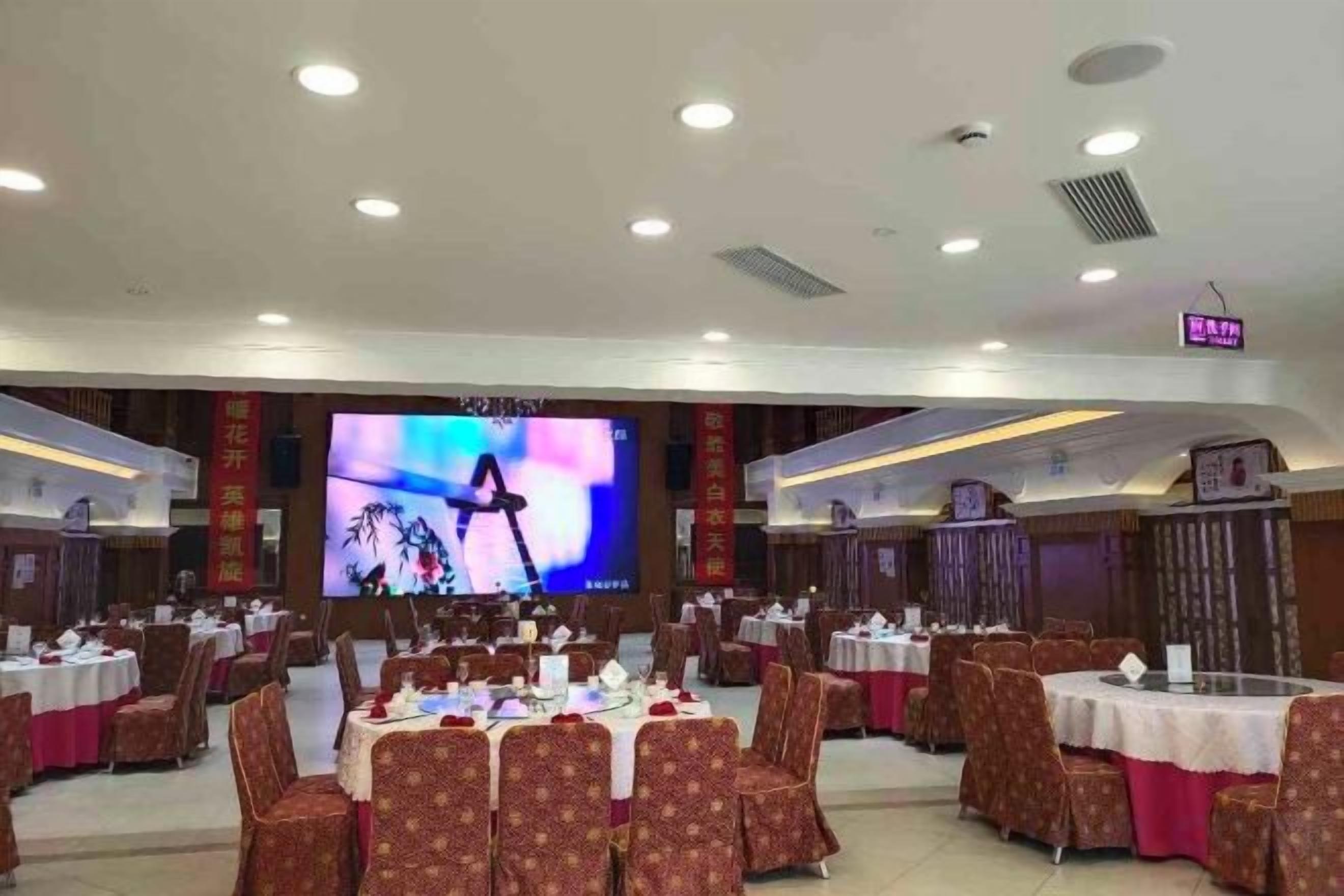 A banquet hall with multiple round tables, chairs, and a large screen displaying an image.