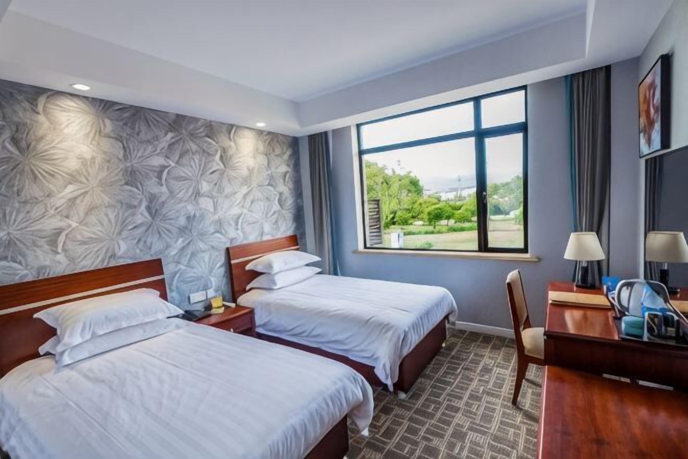 Camera d'albergo con due letti, una scrivania, una sedia, una finestra vista e una parete decorata.