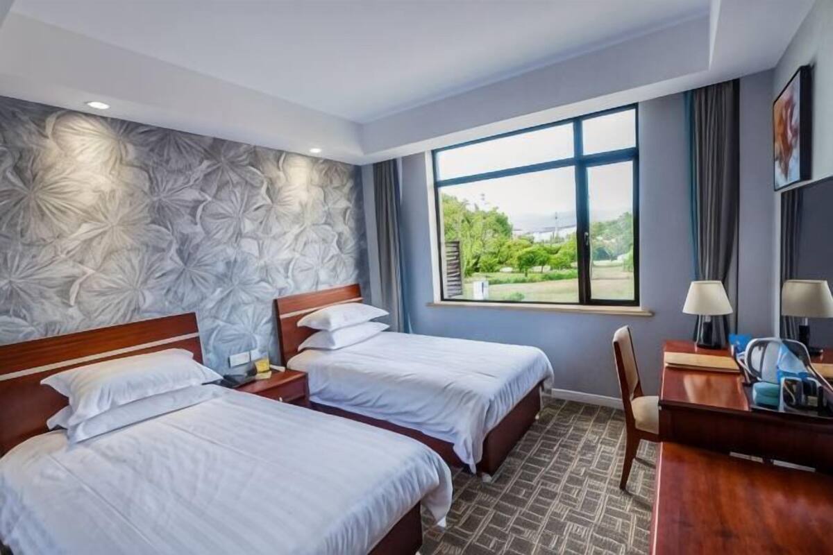 Een hotelkamer met twee bedden, een bureau, een stoel, een raam met uitzicht en een kamer met een patroon op de muur.