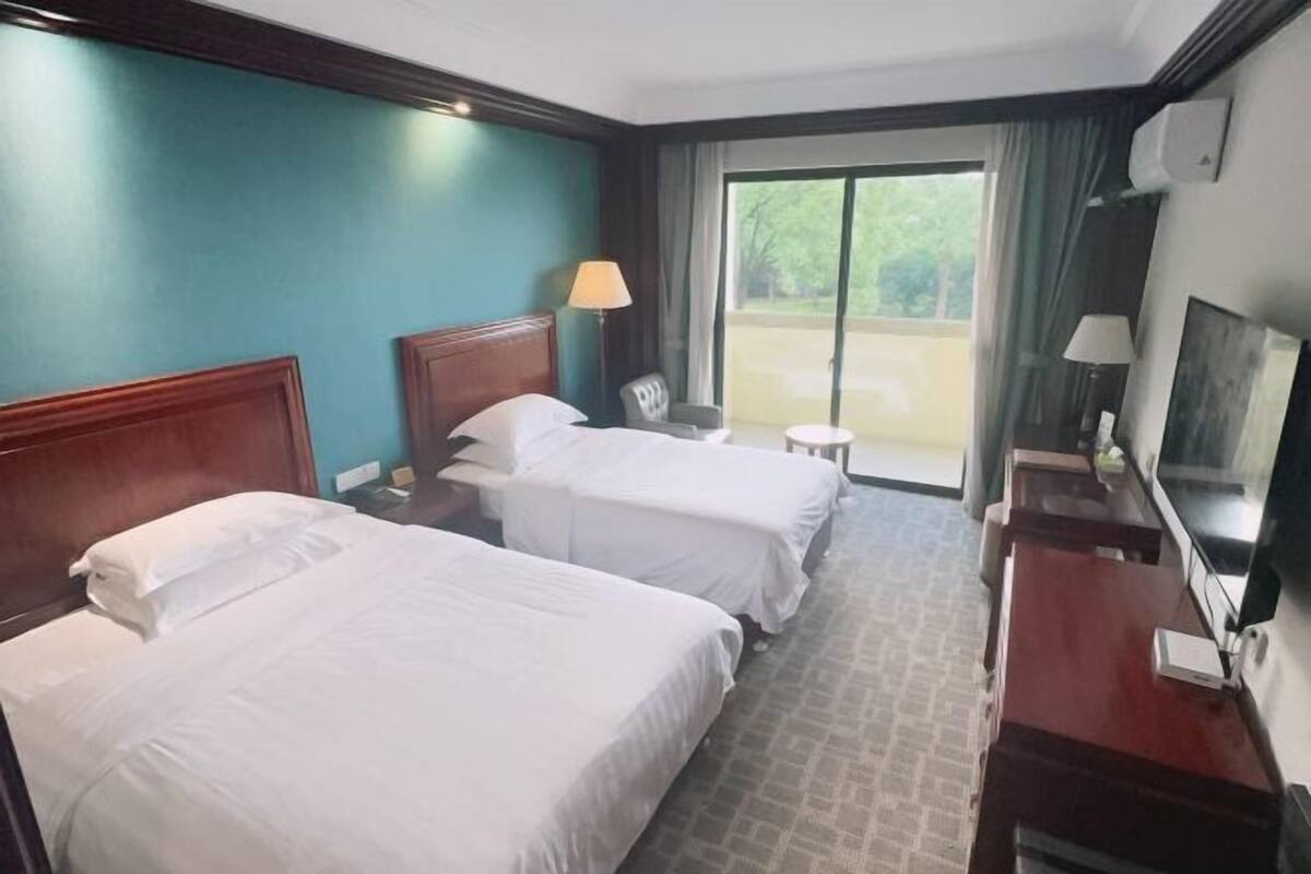 Een hotelkamer met twee bedden, een bureau, een stoel, een televisie en uitzicht op het omliggende landschap.