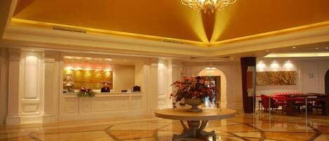 A hotel lobby with a reception desk, a chandelier, and a dining area.