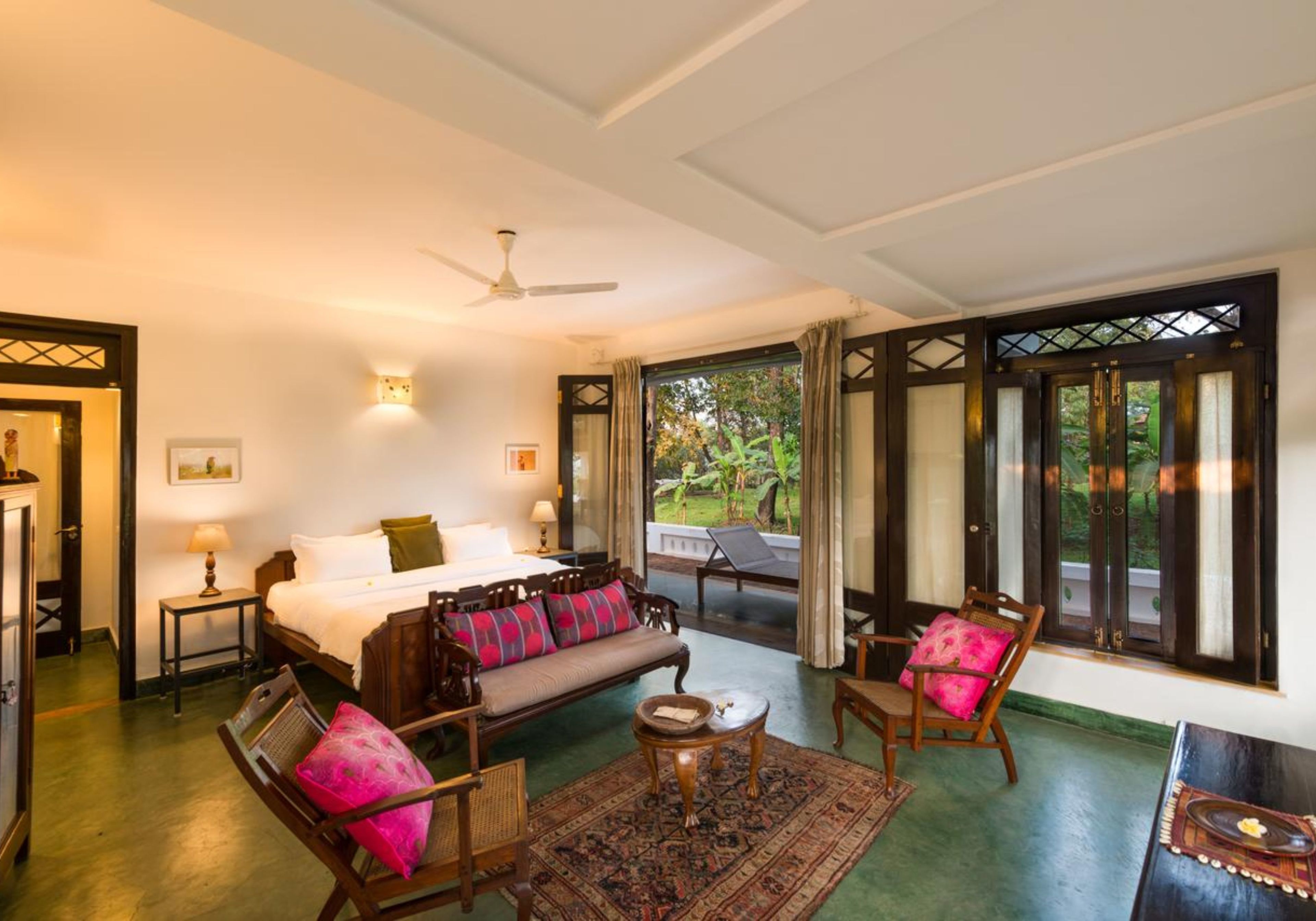 A spacious room with a bed, a sofa, a chair, a small table, and a view of greenery outside.