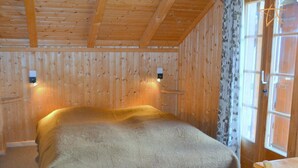 Une pièce de cabane en bois comprenant un lit, une fenêtre avec des rideaux et une table en bois.