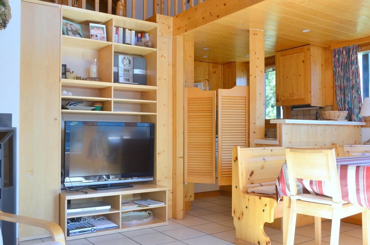 Ein Holzinnenraum mit einem Fernseher auf einem Standfuß, einem Esstisch mit Stühlen und Holzschränken.