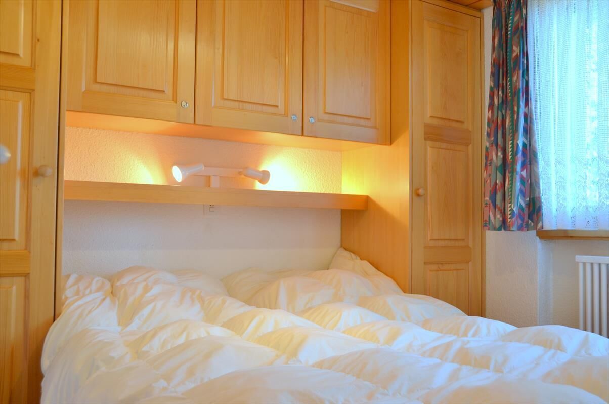 Une chambre à coucher avec un lit, des armoires en bois et une fenêtre avec des rideaux.