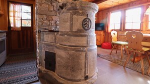 Ein Kamin aus Stein mit Schornstein, ein Holzes Esstisch mit Stühlen und eine Küchenzeile mit Herd und Schränken.
