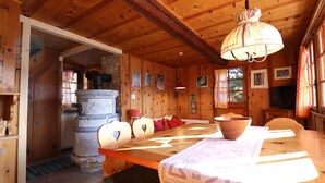 Ein Interieur einer Holzhütte mit einem Esstisch, Stühlen, einem Steinkocher und einem Fernseher.
