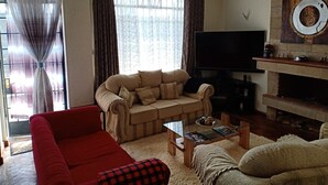 A living room with a beige sofa, a red armchair, a glass coffee table, a flat-screen TV, and a fireplace.