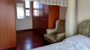 A bedroom with a bed, a chair, wooden wardrobe, and a window with a view.