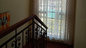 A staircase with a wooden handrail and black metal balusters, leading to a room with a large window covered by sheer white curtains with a diamond pattern.