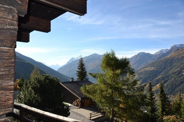 A mountain lodge with a wooden exterior, a covered deck, and a view of surrounding mountains.