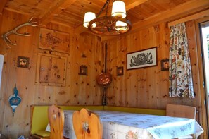 Interior de una cabaña de madera con una mesa de comedor, sillas, una araña y adornos en las paredes.