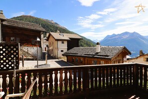 A mountain village with traditional wooden buildings, a balcony with a lattice design, and a view of the mountains. - Outside: chalet on 3 floors ideally located in the centre of the village with entrance on the 1st fl (St-Luc)