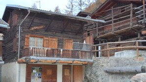 A rustic wooden building with a balcony, stone steps, and a signboard.