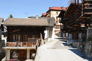 A narrow street with traditional wooden buildings, a wooden bench, and a stone wall. - Outside: chalet on 3 floors ideally located in the centre of the village with entrance on the 1st fl (St-Luc)