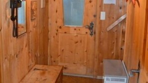 A wooden cabin interior with a bench, a door with a frosted glass panel, a heater, and a hanging light fixture.