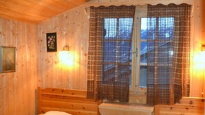 A wooden cabin room with two beds, a window with plaid curtains, and wall-mounted lights.