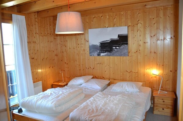 A wooden-paneled room with two beds, a hanging lamp, a nightstand, and a framed picture on the wall.