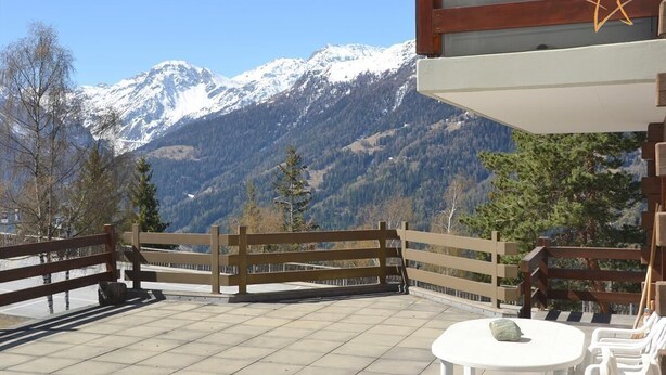 Una terraza con vistas a montañas nevadas, barandas de madera y mobiliario exterior.