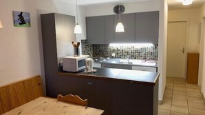 Una cocina compacta con microondas, tostadora y lavamanos. Hay una mesa de comedor de madera y sillas.