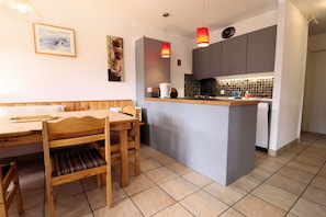 Una cocina compacta con una isla central, una mesa de comedor con sillas y un refrigerador pequeño.