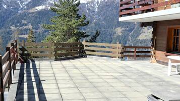 Eine Terrasse mit Holzzaun, Steinboden und Blick auf schneebedeckte Berge.