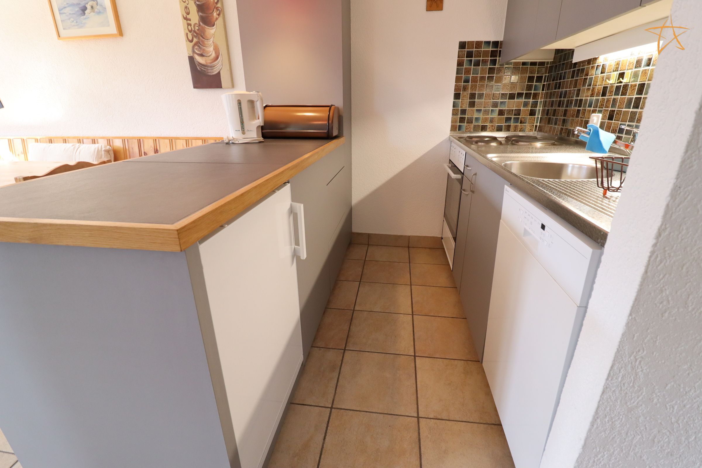 Eine kleine Küche mit einer Holzauskładung, einem Toaster, einer Spüle und einer gefliesten Rückwand.
