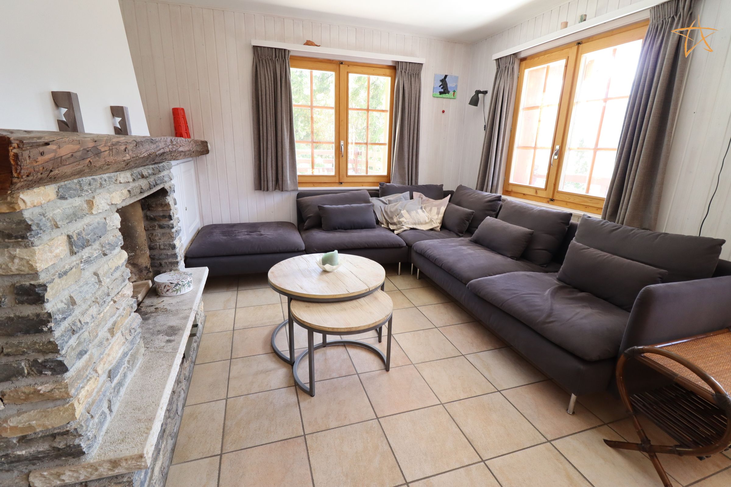 Ein Wohnzimmer mit Kamin aus Stein, einem Ecksofa, einem runden Couchtisch und einem Korbstuhl.