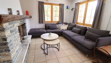 Ein Wohnzimmer mit Kamin aus Stein, einem Ecksofa, einem runden Couchtisch und einem Korbstuhl.