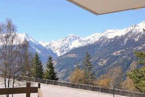 A mountain view from a balcony with a wooden railing, a clear sky, and snow-capped peaks in the distance. - Beautiful apartment with exceptional terrace facing SouthExterior: 1st floor apartment with large so (St-Luc)