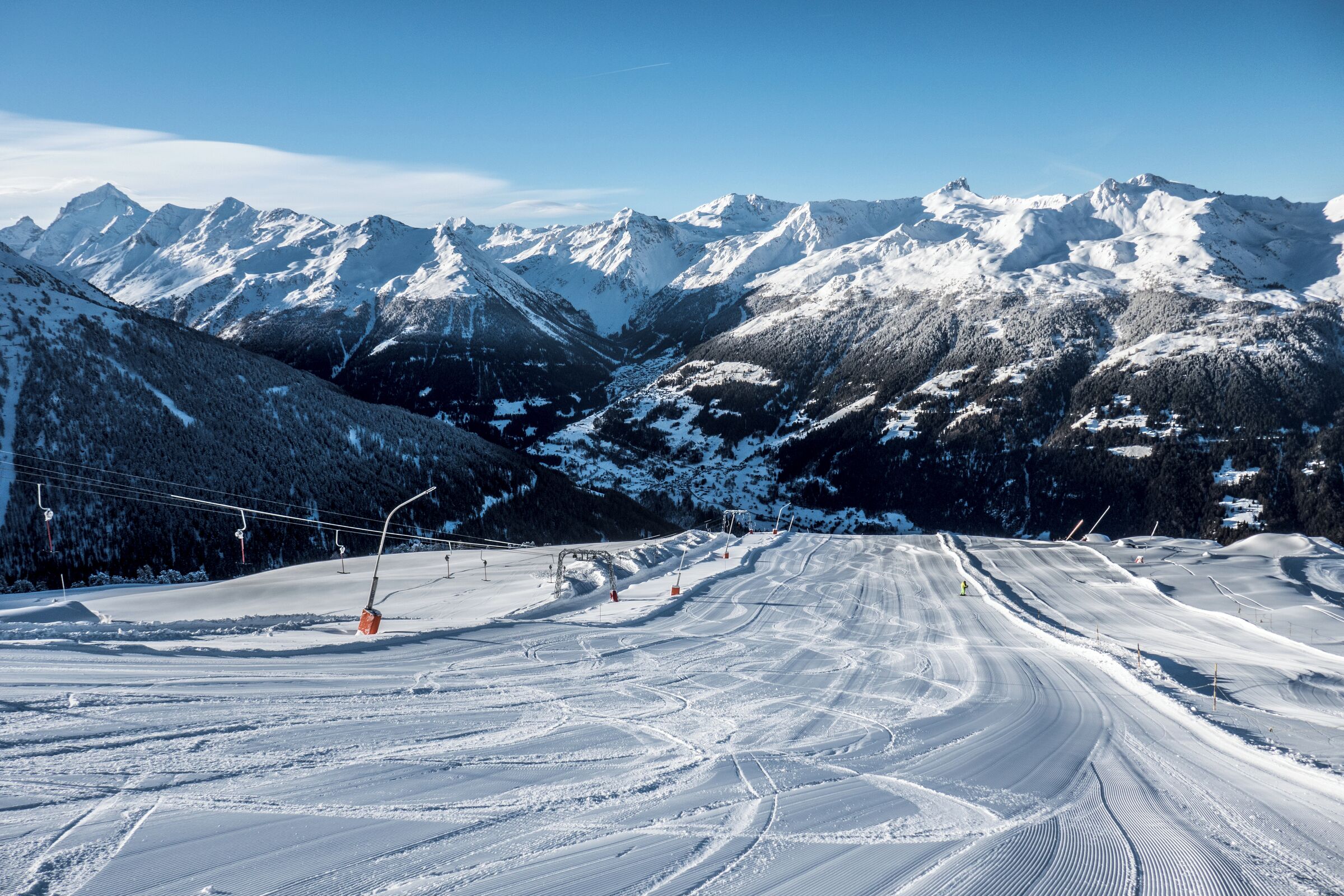 A snow-covered ski slope with ski lifts and mountains in the background.