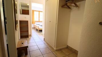Ein schmaler Flur mit einer hölzernen Sitzbank, einem Kleiderschrank und einem Bett mit einem Fenster im Hintergrund.