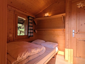Ein Zimmer in einer Holzhütte mit einem Bett, einem Fenster mit Vorhängen und einer sternförmigen Leuchte.