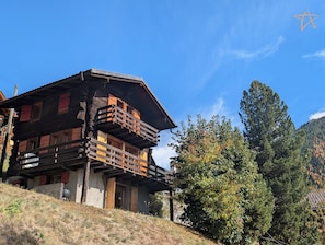 Eine hölzerne Chalet mit mehreren Balkonen und rustikalem Design, umgeben von Bäumen und blauem Himmel.