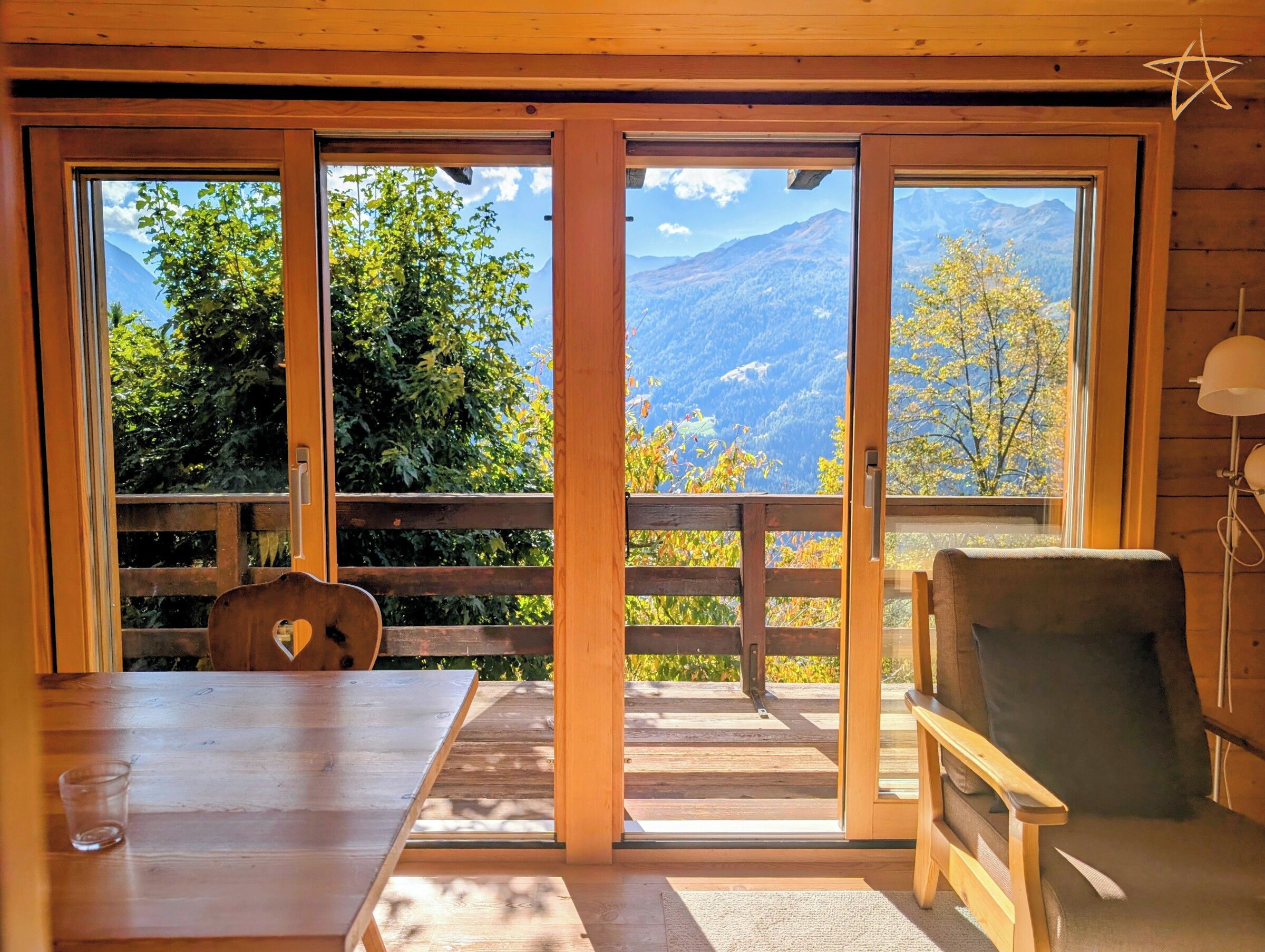 A room with a wooden table, a chair, and a view of mountains through large glass doors.